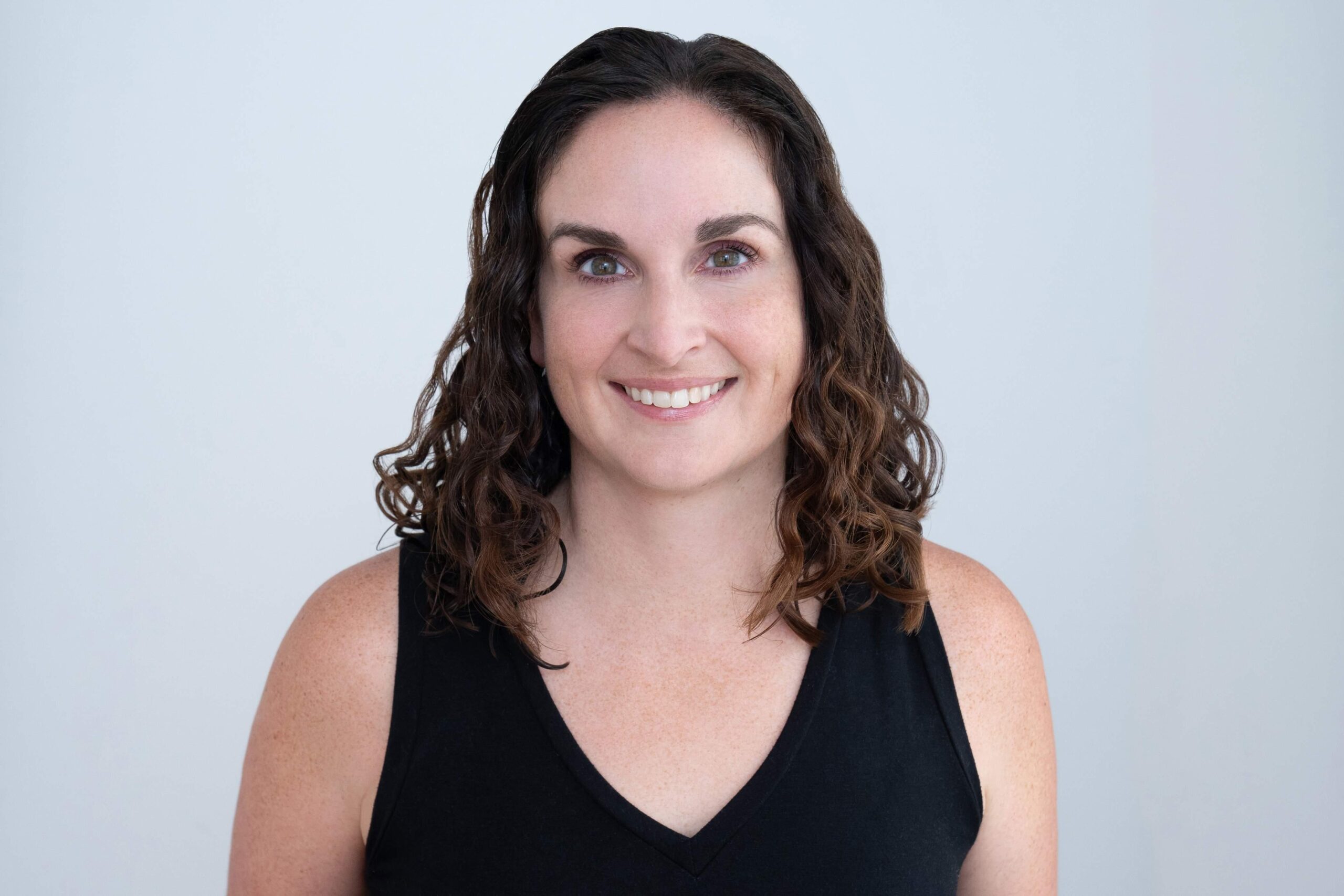 Headshot of Jen Ladson, an instructor at Novo Fitness Studio. Jen wears a black tank top. Her long brown hair cascades over her shoulders as she smiles at the camera.