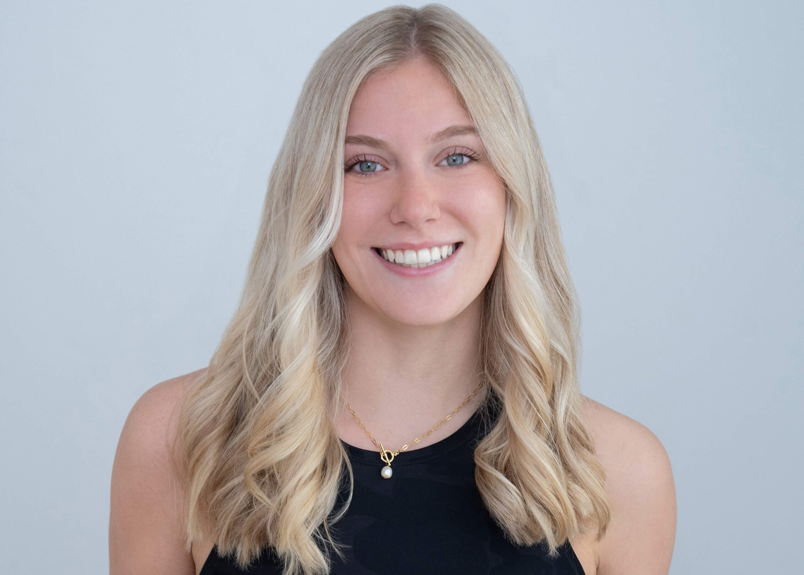 Headshot of Jules Myers, an instructor at Novo Fitness Studio. Jules wears a black tank top. Her long blonde hair cascades over her shoulders as she smiles at the camera.