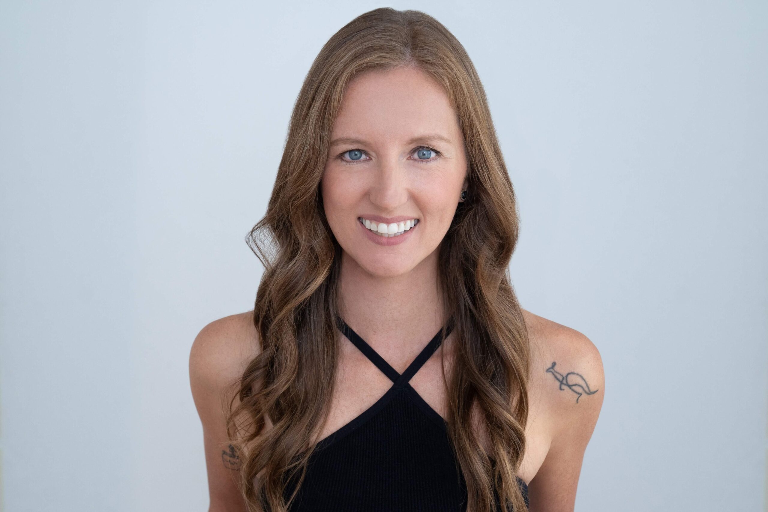 Headshot of Kristain Macphail, an instructor at Novo Fitness Studio. Kirstain wears a black halter-style workout top. Her long brwon hair cascades over her shoulders as she smiles at the camera.